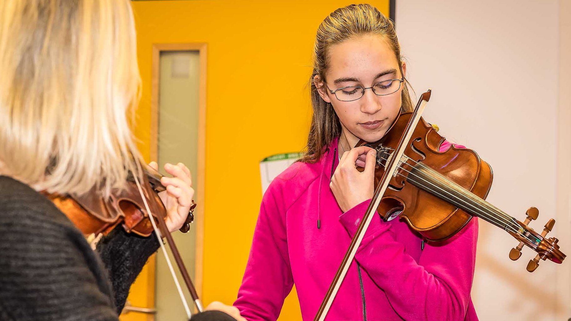 Musiklehrerin und jugendliche Schülerin stimmen gemeinsam ihre Violinen