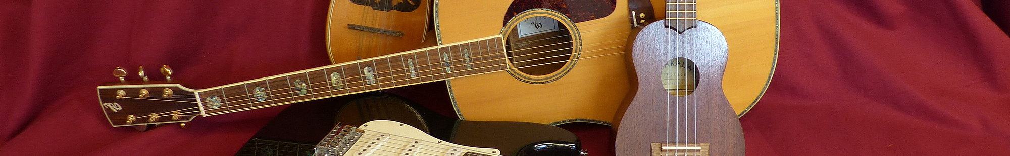 Eine Laute, akustische Gitarre, Ukulele und eine E-Gitarre liegen auf einem rot gedecktem Tisch